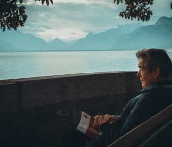 medicare aged man sitting near water and mountains